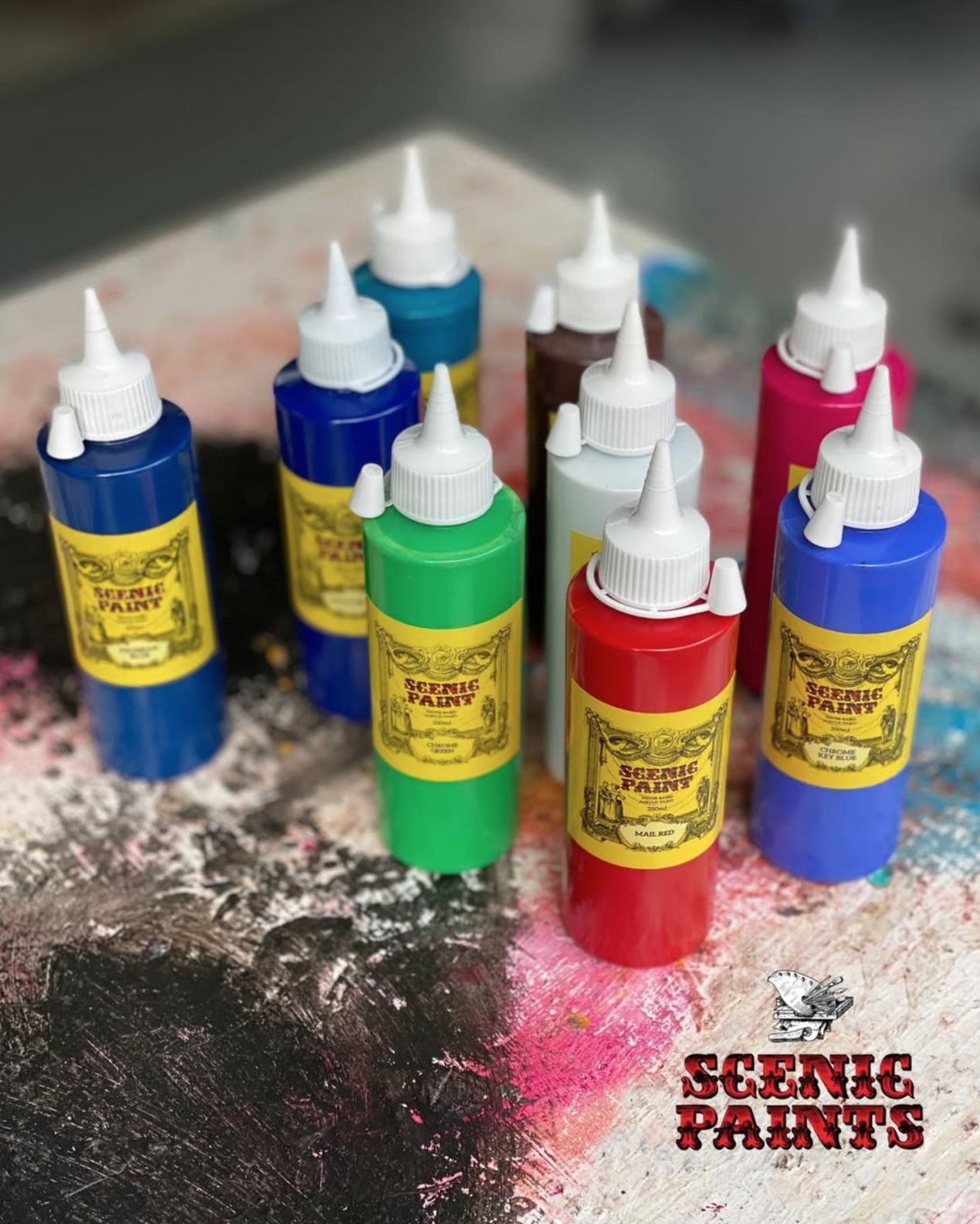 Bottles of scenic paint in primary colours on a paint-splattered bench