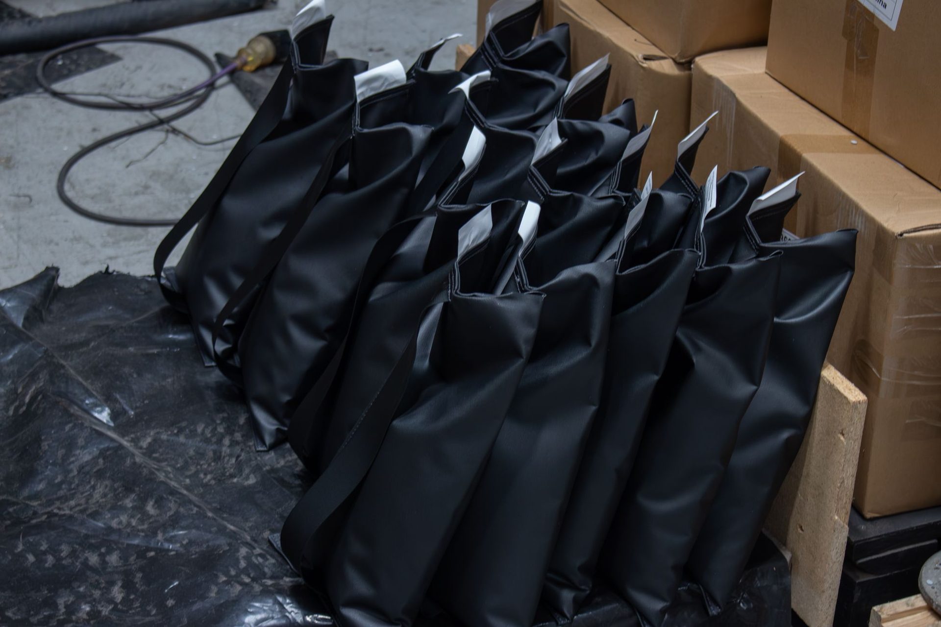 A row of black shotbags standing on plastic sheeting beside stacked cardboard cartons in a warehouse