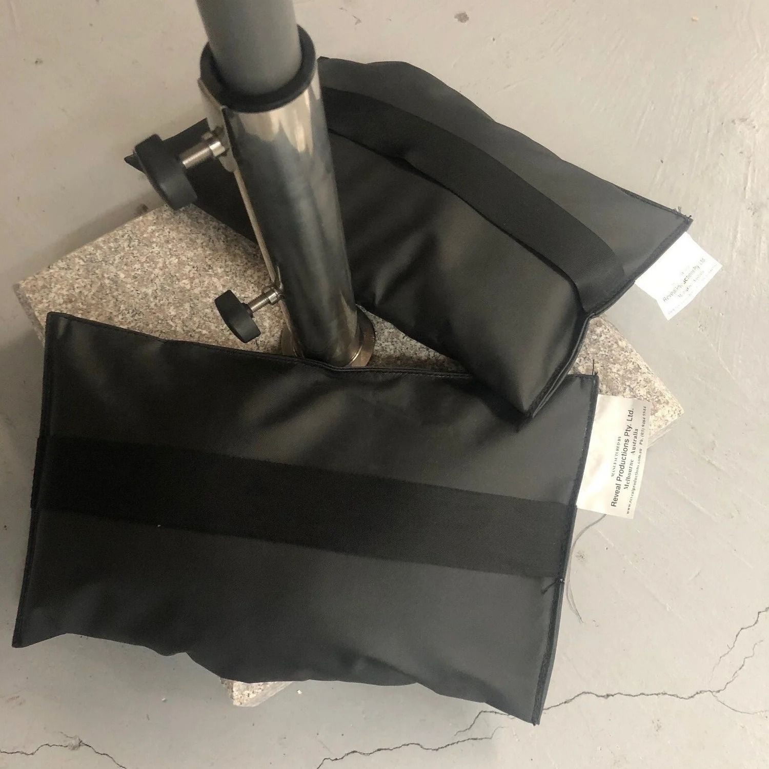 Two black shotbags with Reveal labels weighting the base of a stand on a concrete floor
