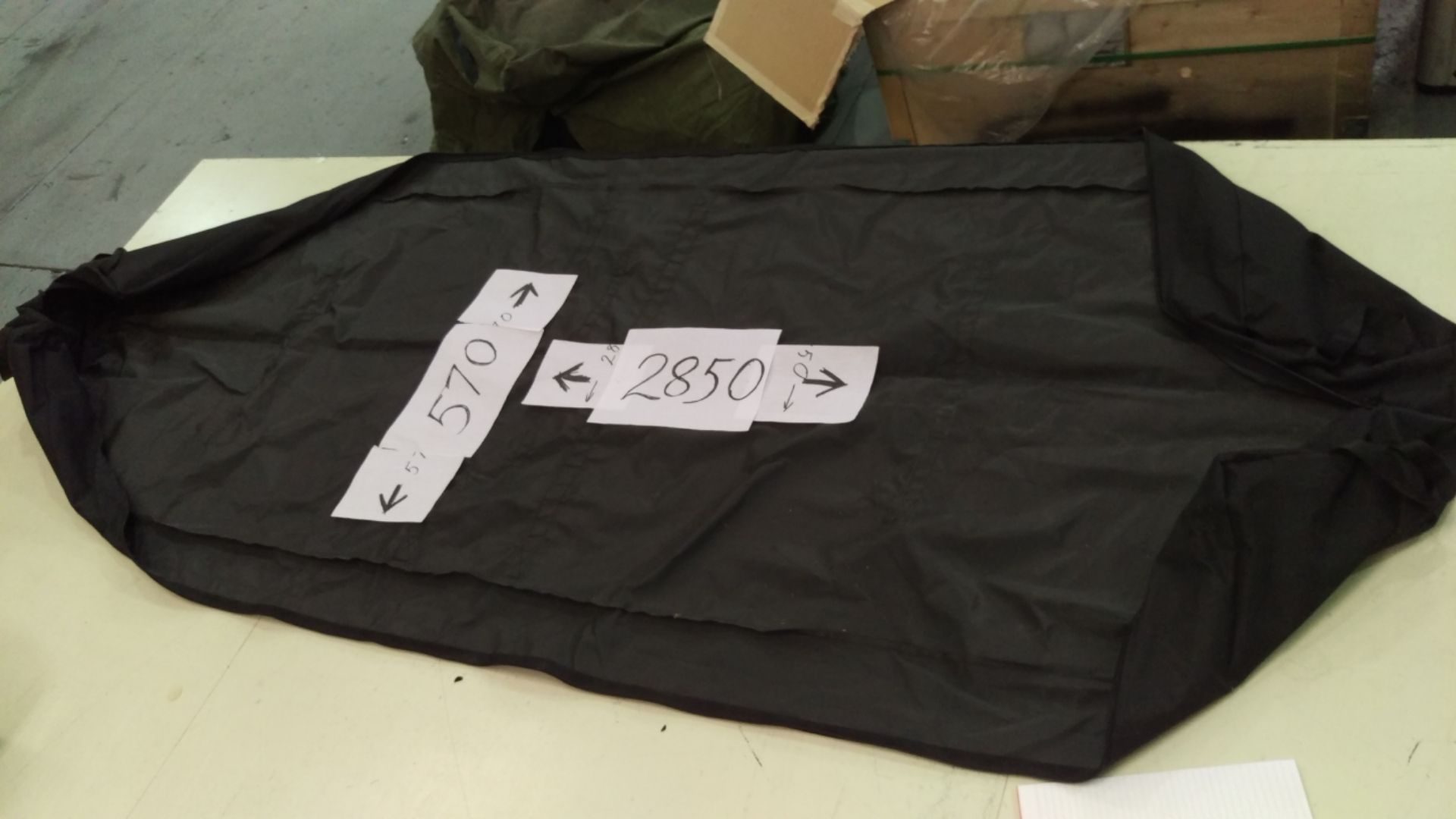 A black carry bag laid on a workshop bench with paper labels marking its finished sizes, 570 and 2850