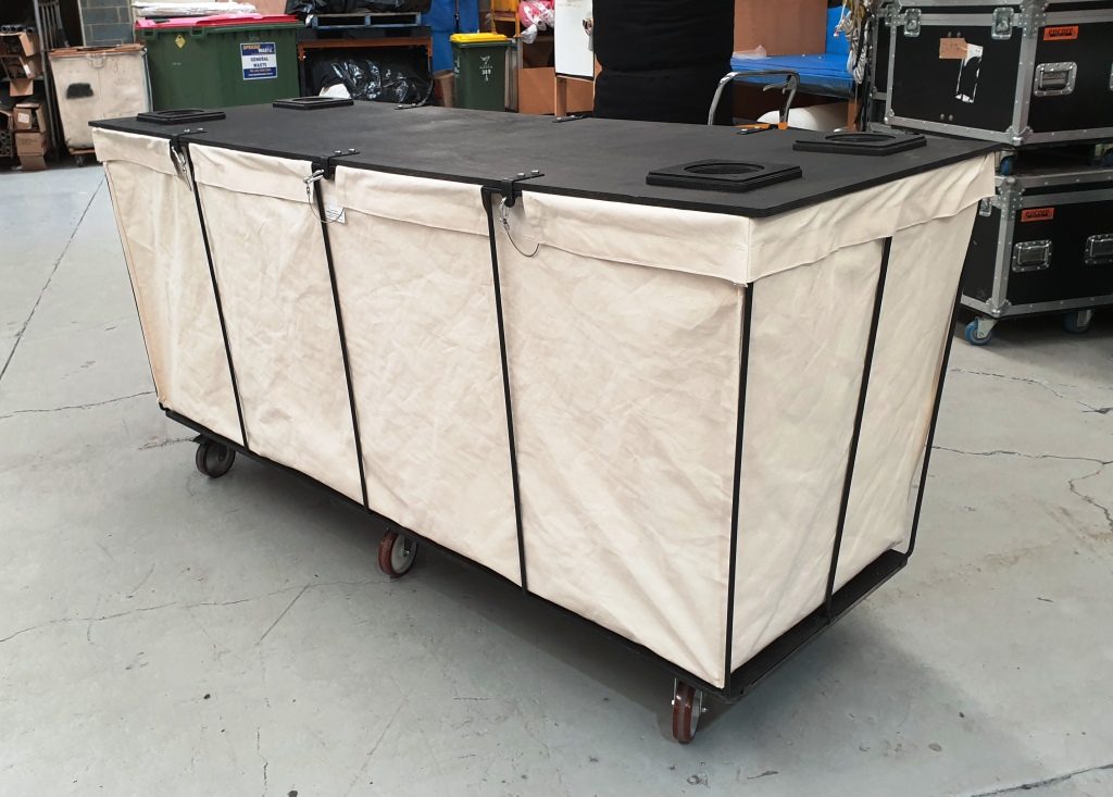 Lidded canvas storage hamper on castors in a warehouse, road cases stacked behind it