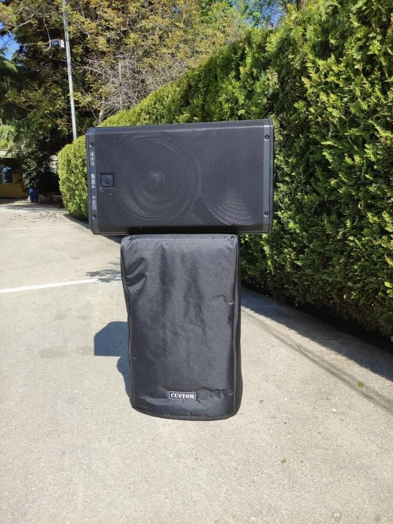 A bare speaker lying across the top of a second speaker that wears its fitted black cover