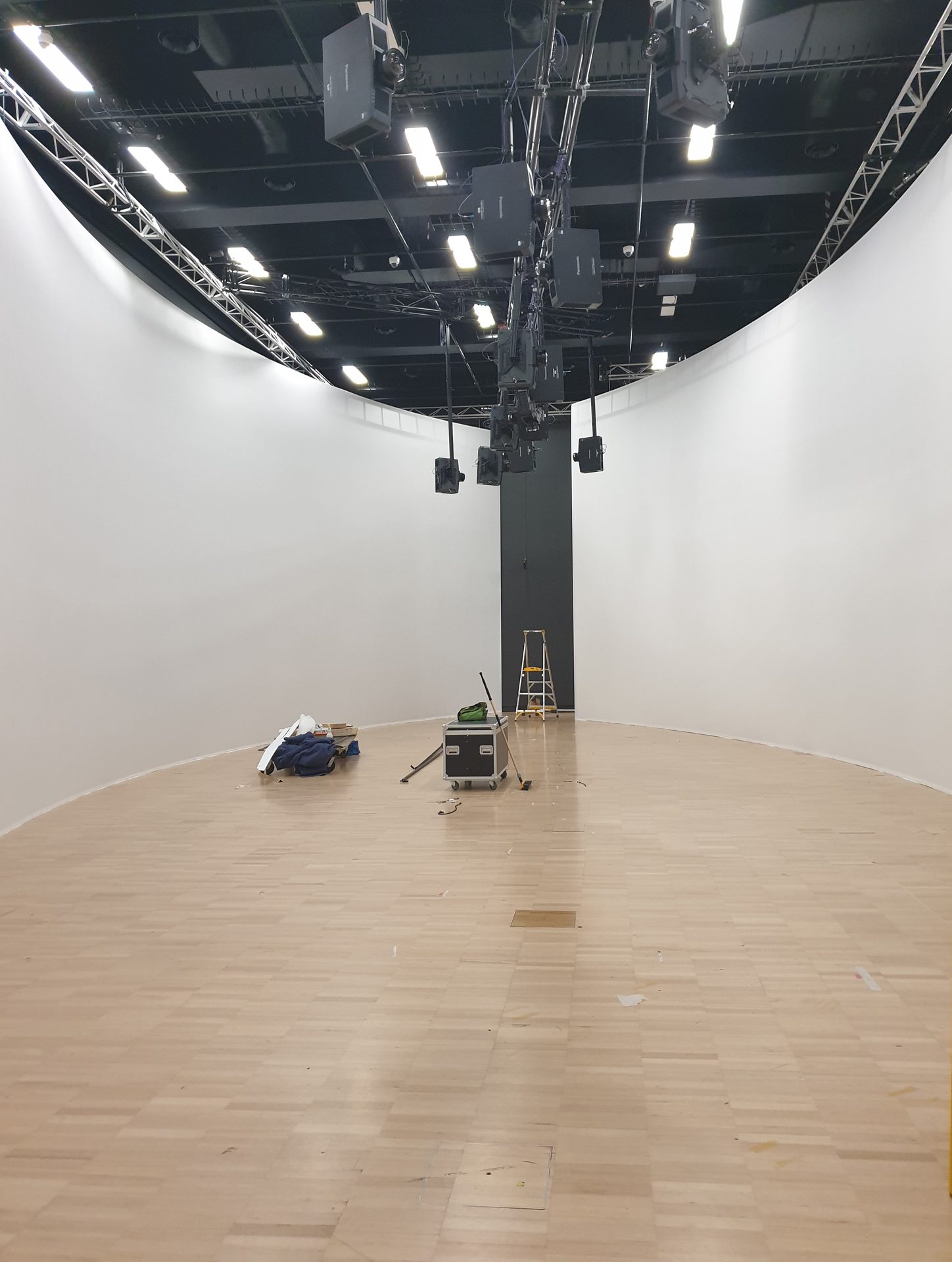 A bare white curved cyclorama wrapping an empty studio with a timber floor, lighting rig overhead