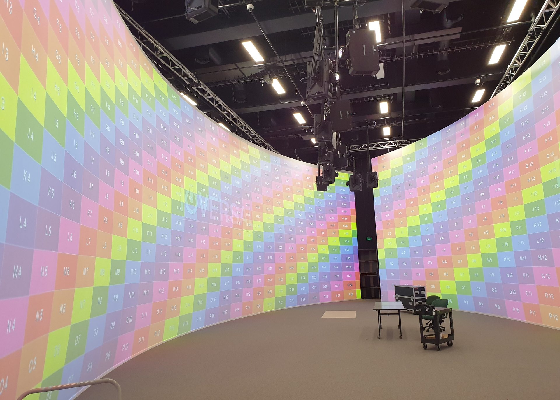 A wide curved white cyclorama wrapping a projection studio, lit edge to edge with a projected colour grid