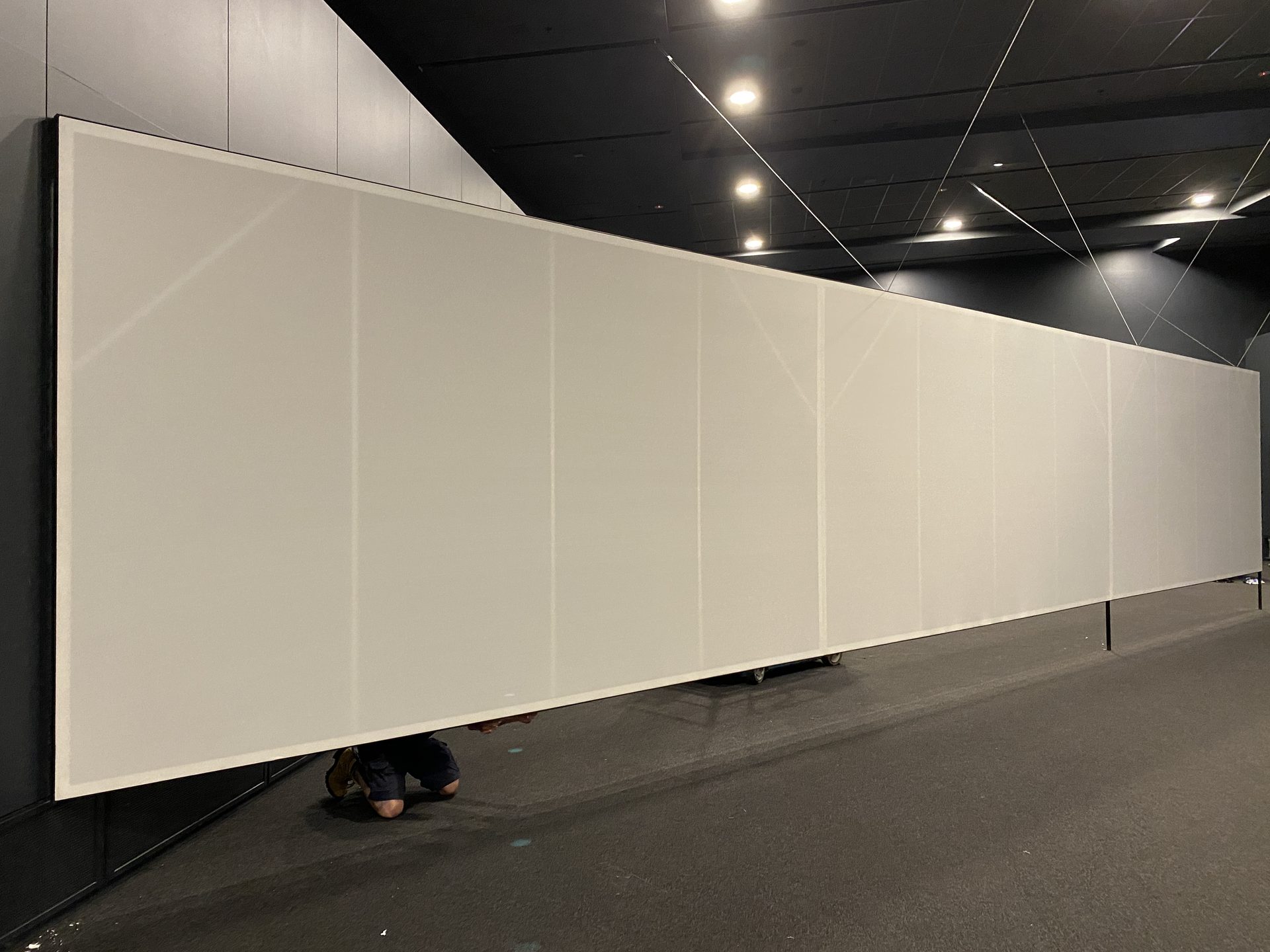 A long white cyclorama wall stretched along a dark venue under downlights