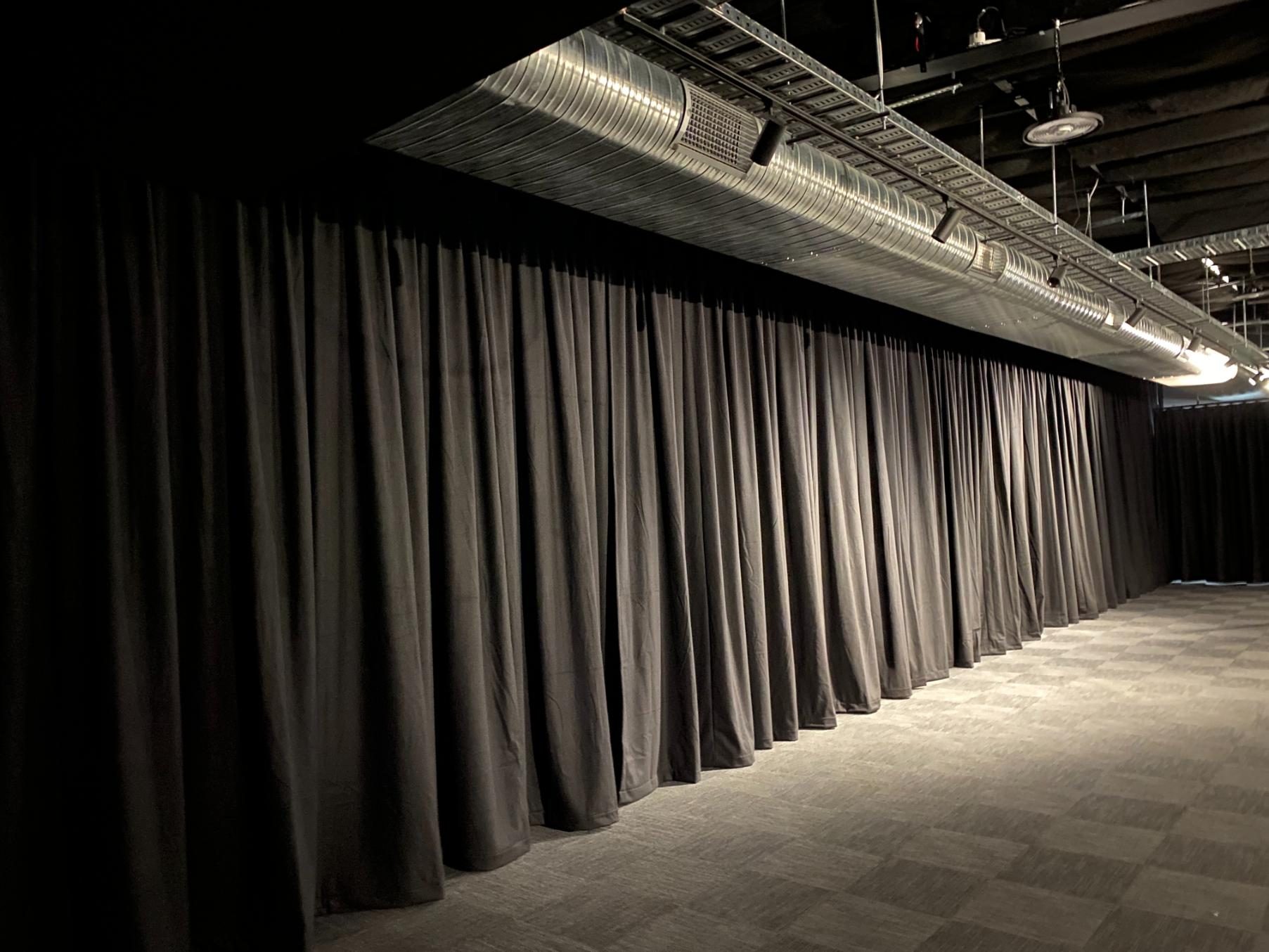 Full-height black drapes run wall to wall beneath exposed ceiling services in a converted studio
