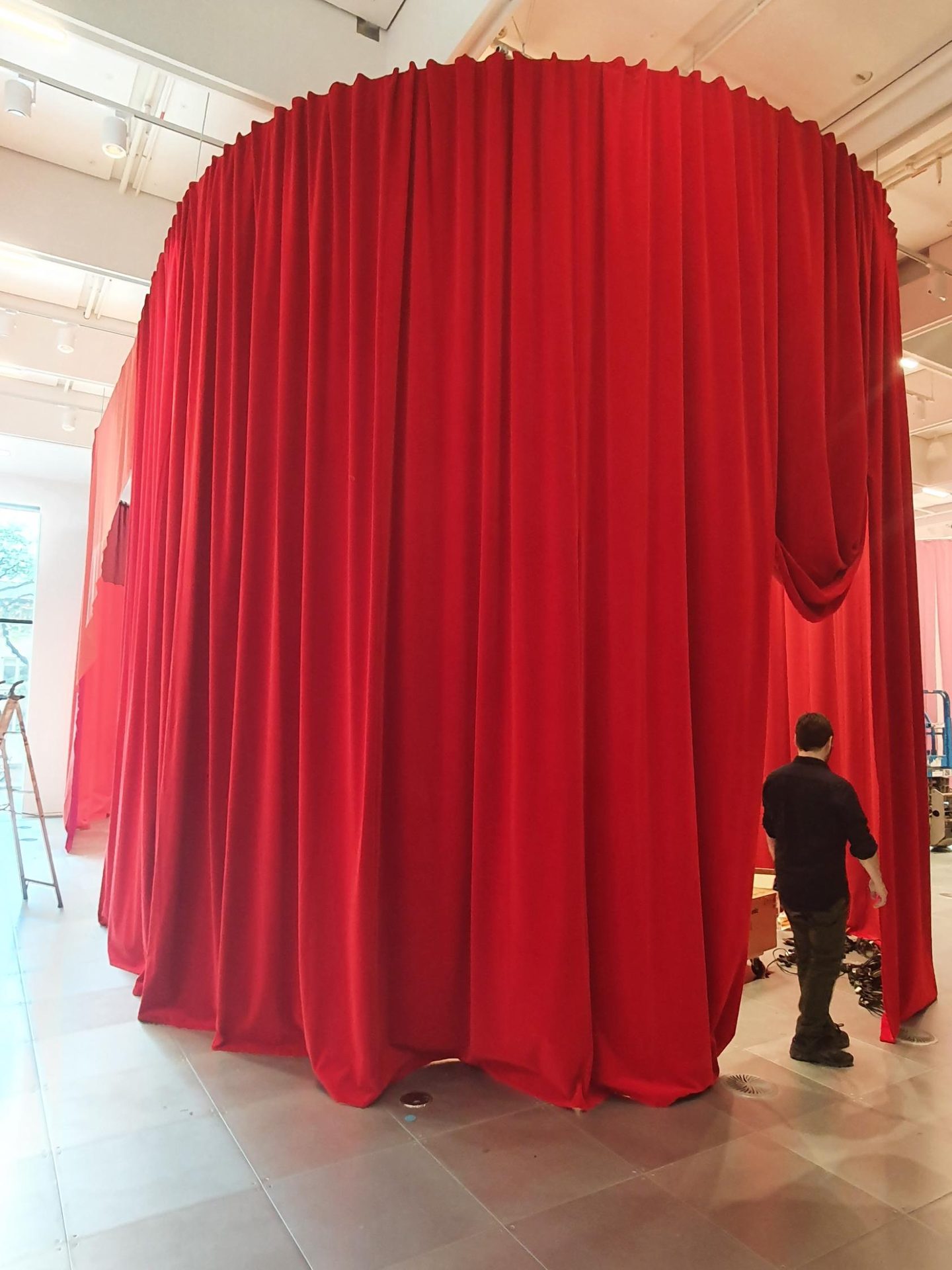 An installer stepping out of a tall round enclosure of red velour drapes in a white room