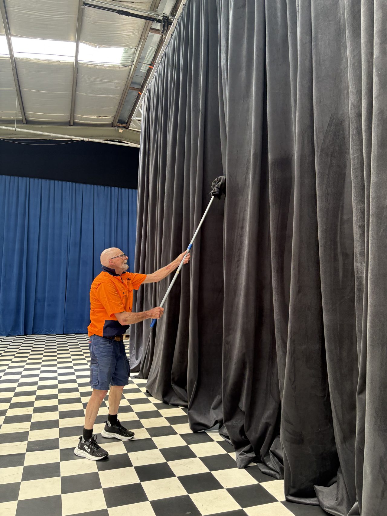 Staff member cleaning a tall grey stage drape