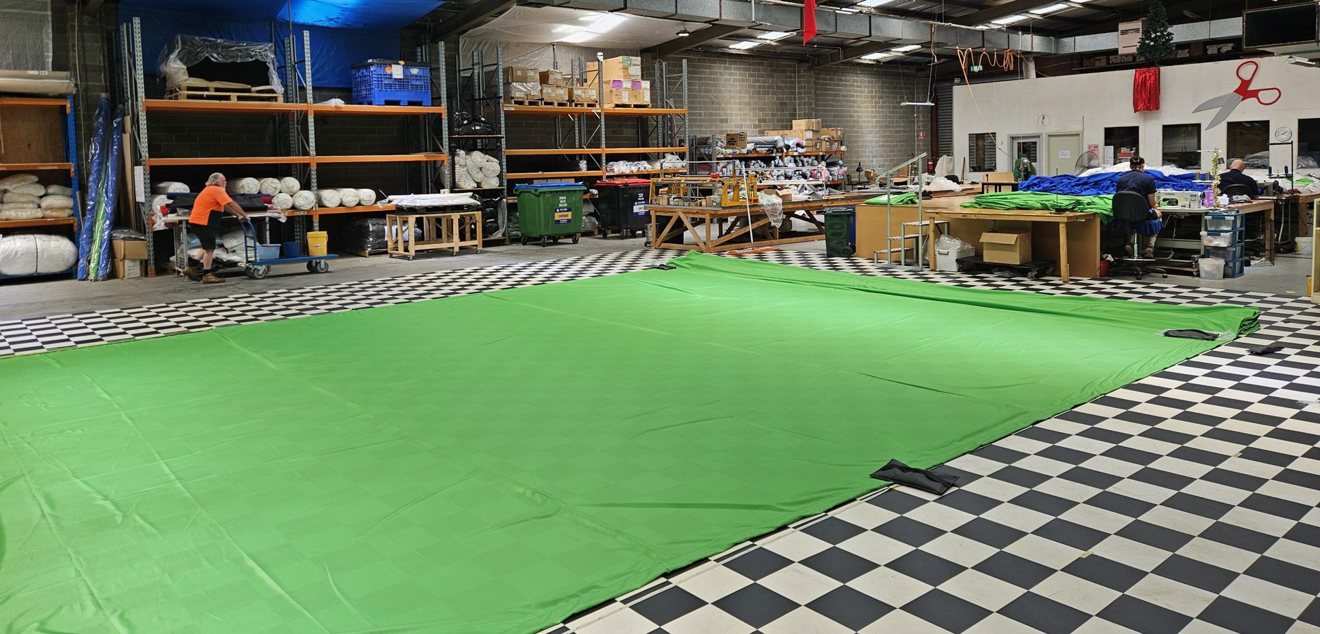 A large green screen cloth laid out across the workshop floor