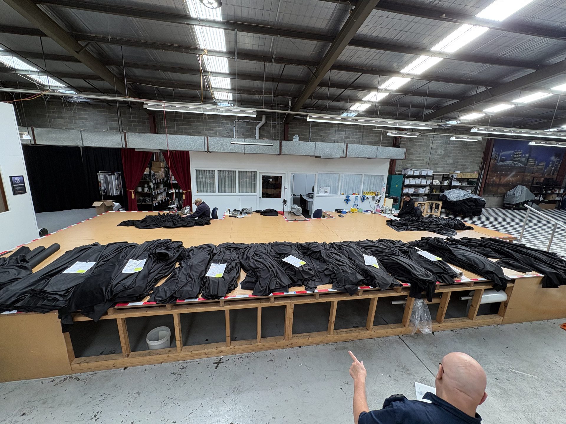 Black velour drapes laid out side by side along a long workshop table, seen from above