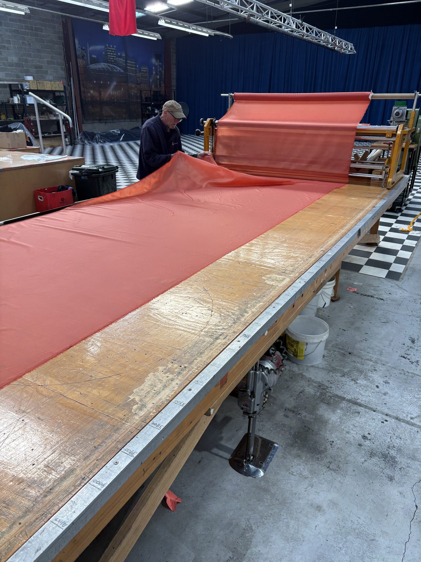 A length of coral-red fabric unrolled down a long cutting table in the workshop, a machinist working at the far end