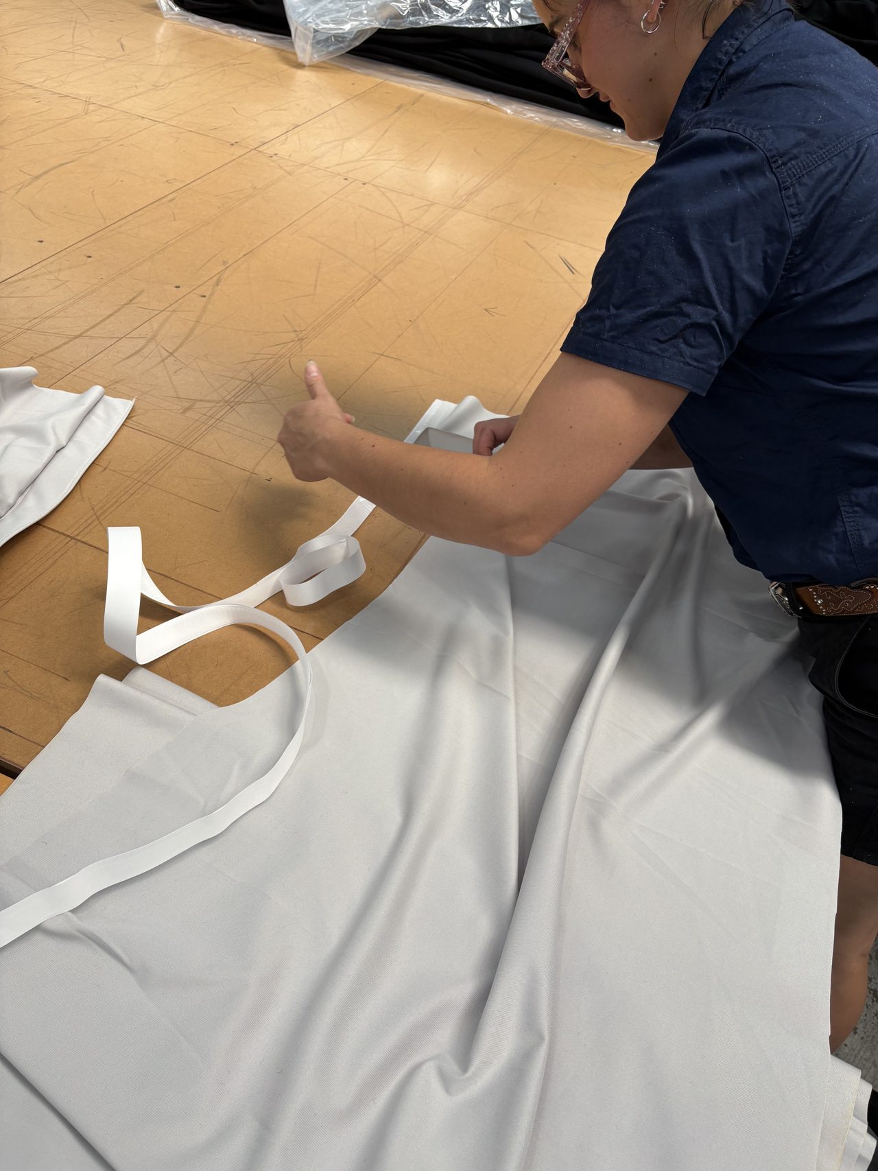 A machinist laying white webbing tape along the edge of a white cloth panel on the cutting table