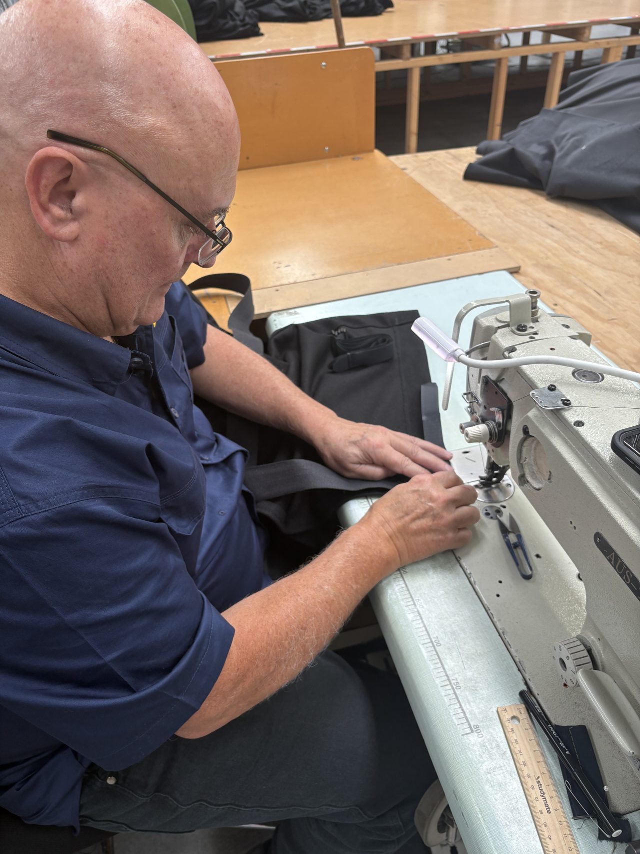 A machinist at an industrial sewing machine stitching a length of black webbing strap