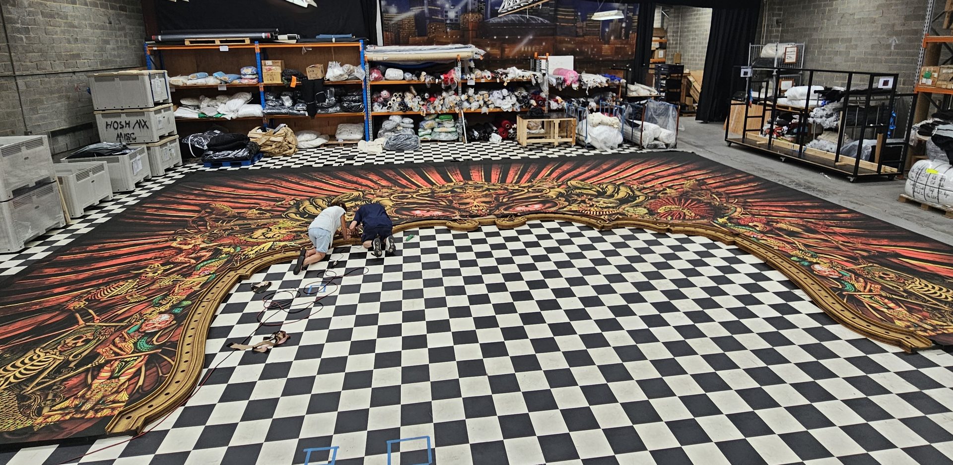 Two makers kneeling on a large ornate cloth of red rays and gold detail spread across the workshop floor
