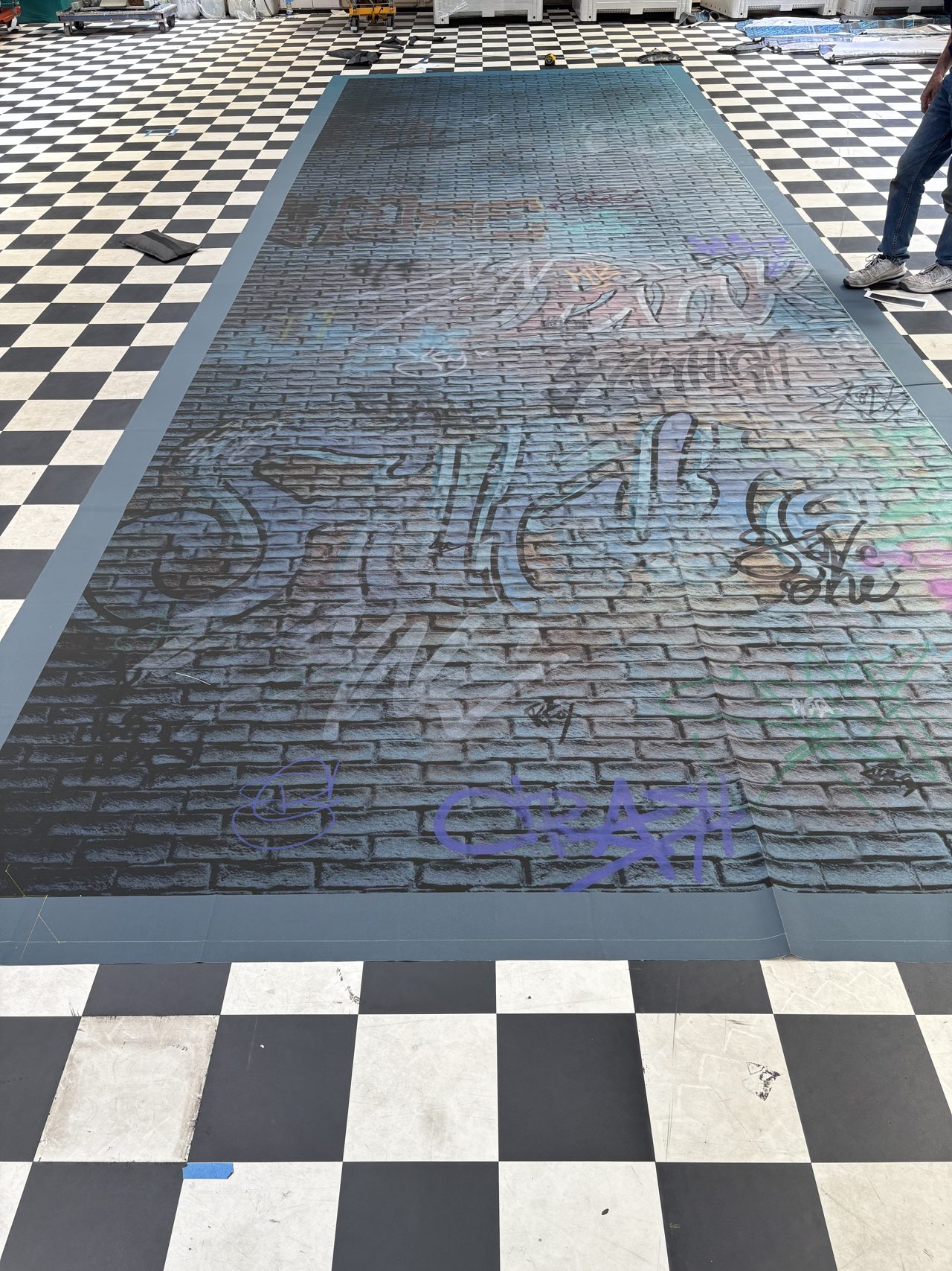 A blue-toned graffiti brick wall cloth laid out on the chequered workshop floor