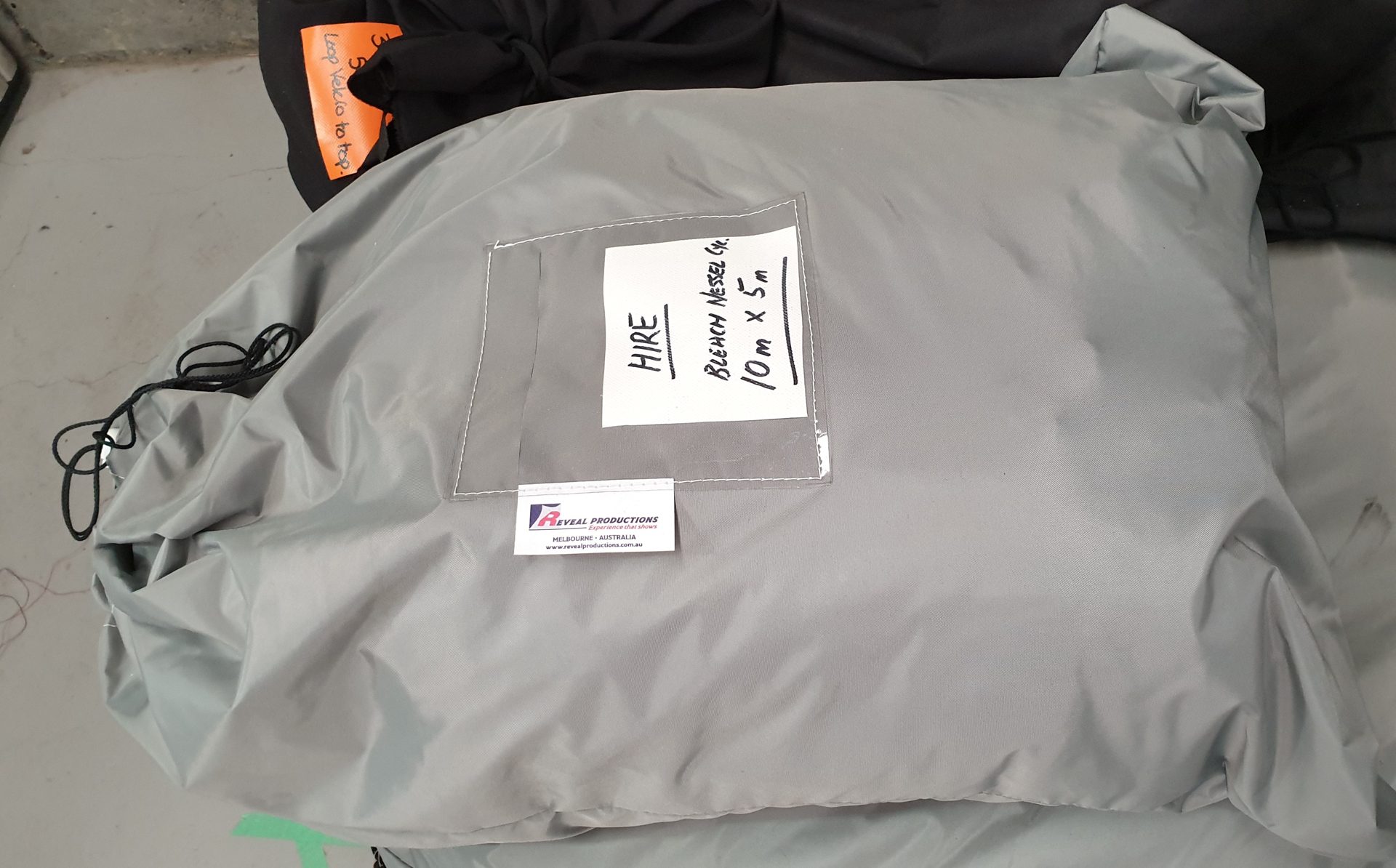 A grey drape storage bag with a hand-written hire label in its card pocket