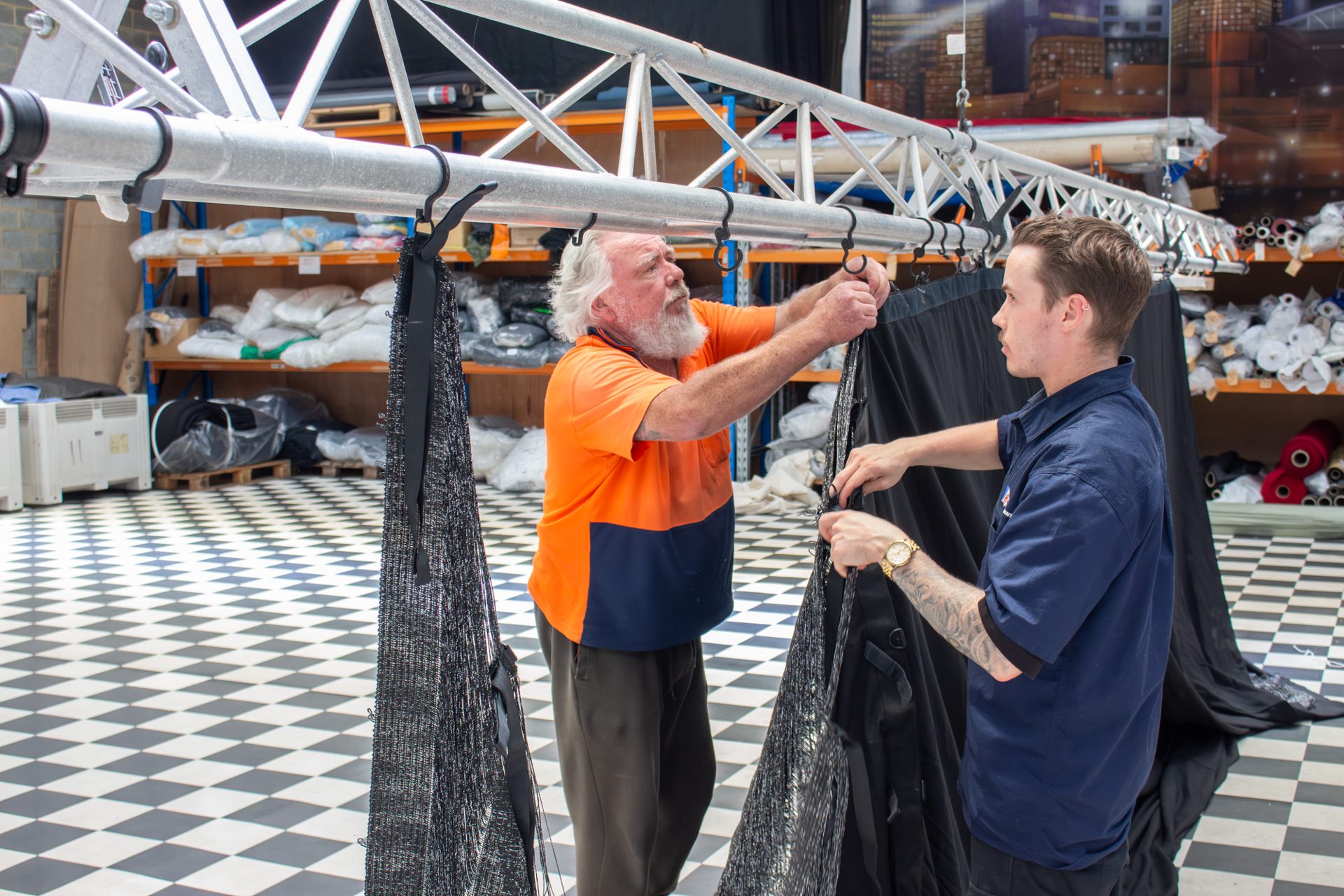 Two crew hanging a black drape from truss in the workshop