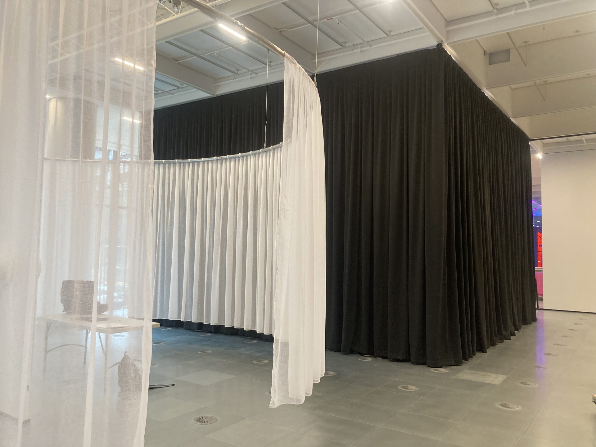 Sheer white and black drapes on curved track dividing an exhibition room