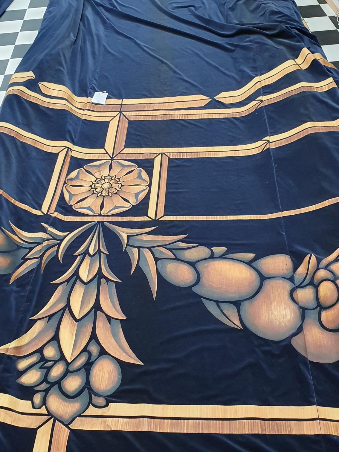 A navy drop with gold Art Deco artwork laid out full length on the chequered workshop floor