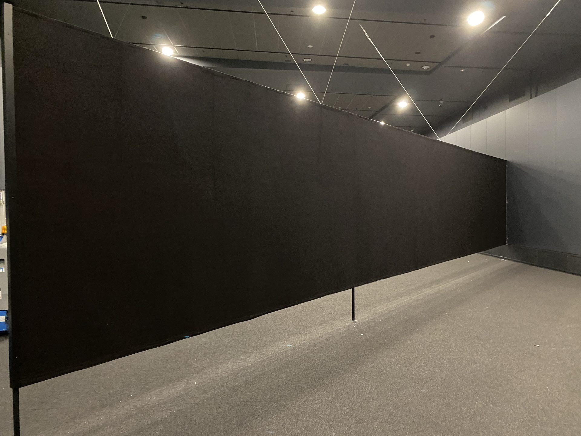 A long wall of black drapes standing in an empty convention hall under downlights