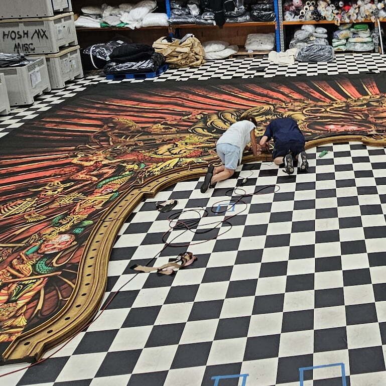 Two Reveal makers working on a printed soft scenery drop laid out across the workshop floor for MJ the Musical