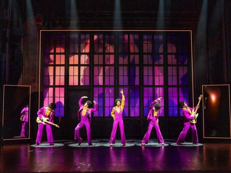 Five performers in magenta suits as the Jackson 5 in the Australian production of MJ the Musical, in front of a glowing factory-window backdrop