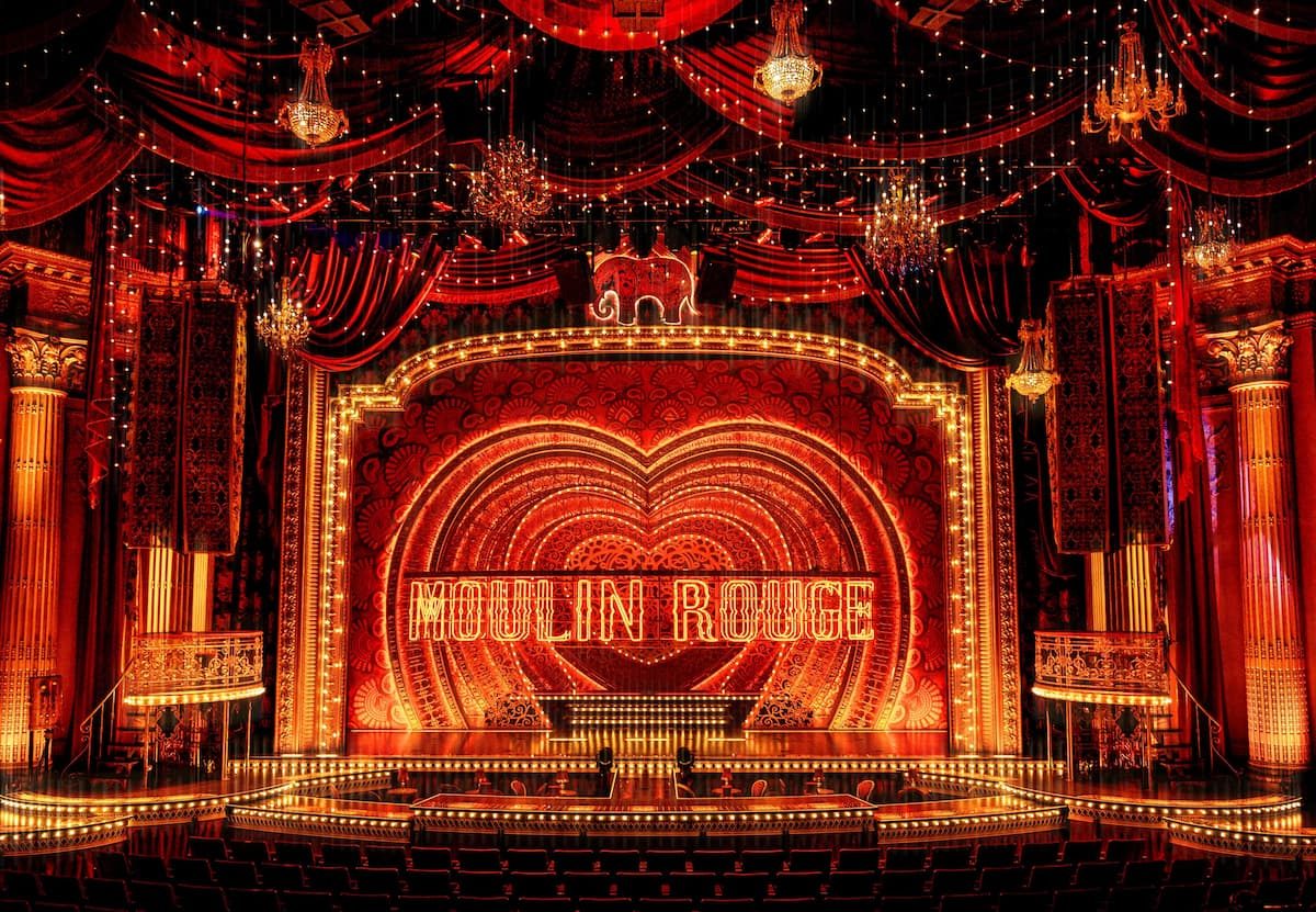The Moulin Rouge! stage framed in red drapery, chandeliers and lit signage
