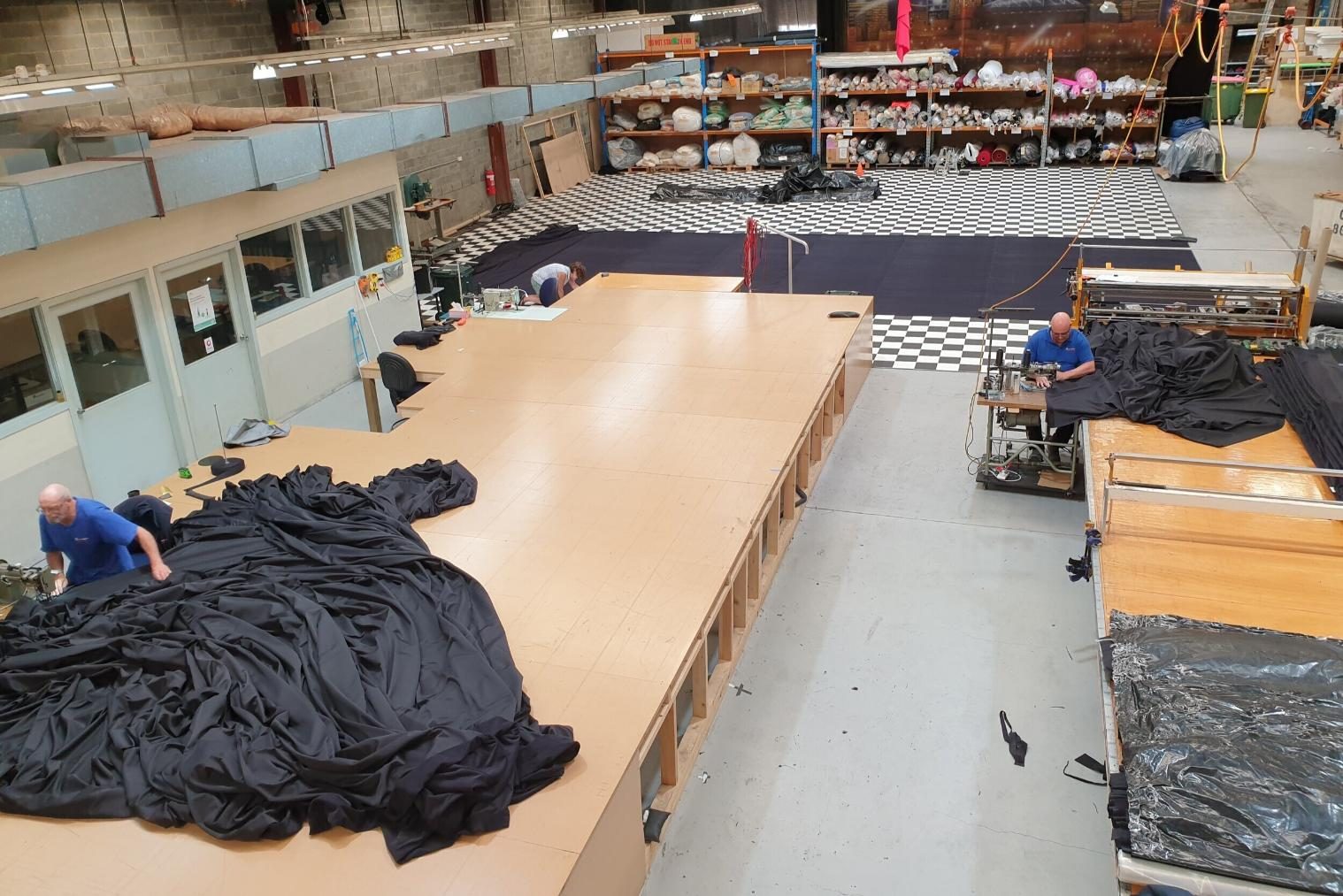 Workshop floor with black masking drapes spread across the cutting tables while two staff work the cloth