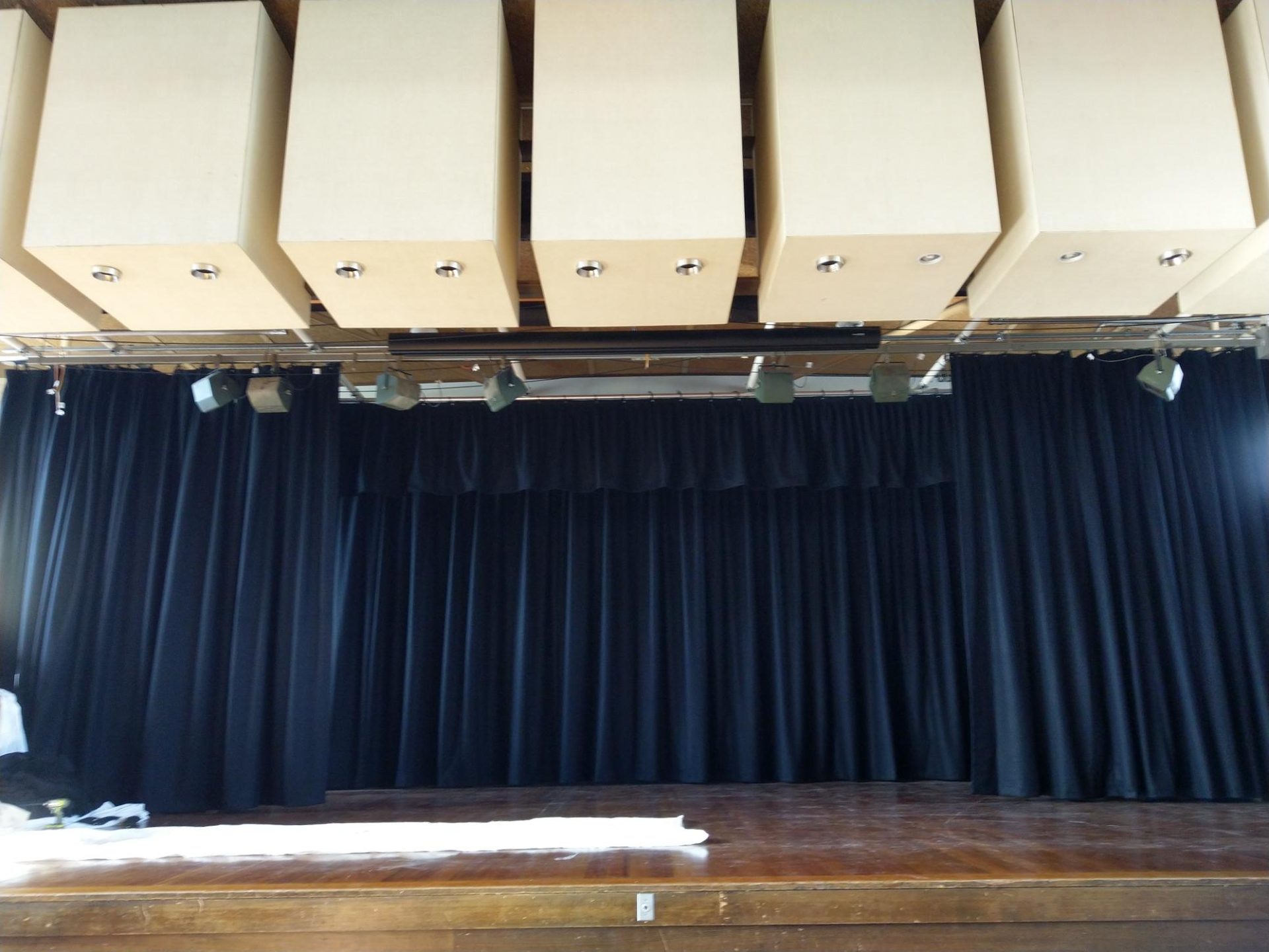A school stage with black travellers drawn open beneath acoustic ceiling panels
