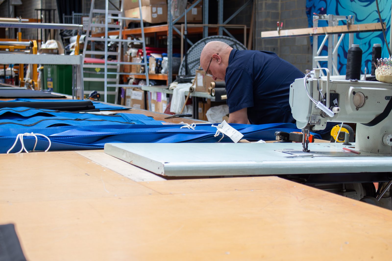 A machinist at an industrial sewing machine feeding blue fabric across the bench