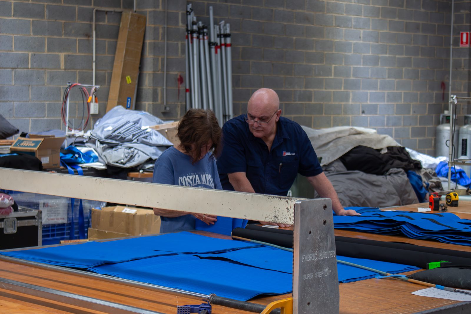 Two machinists checking blue fabric laid along a cutting table in the workshop