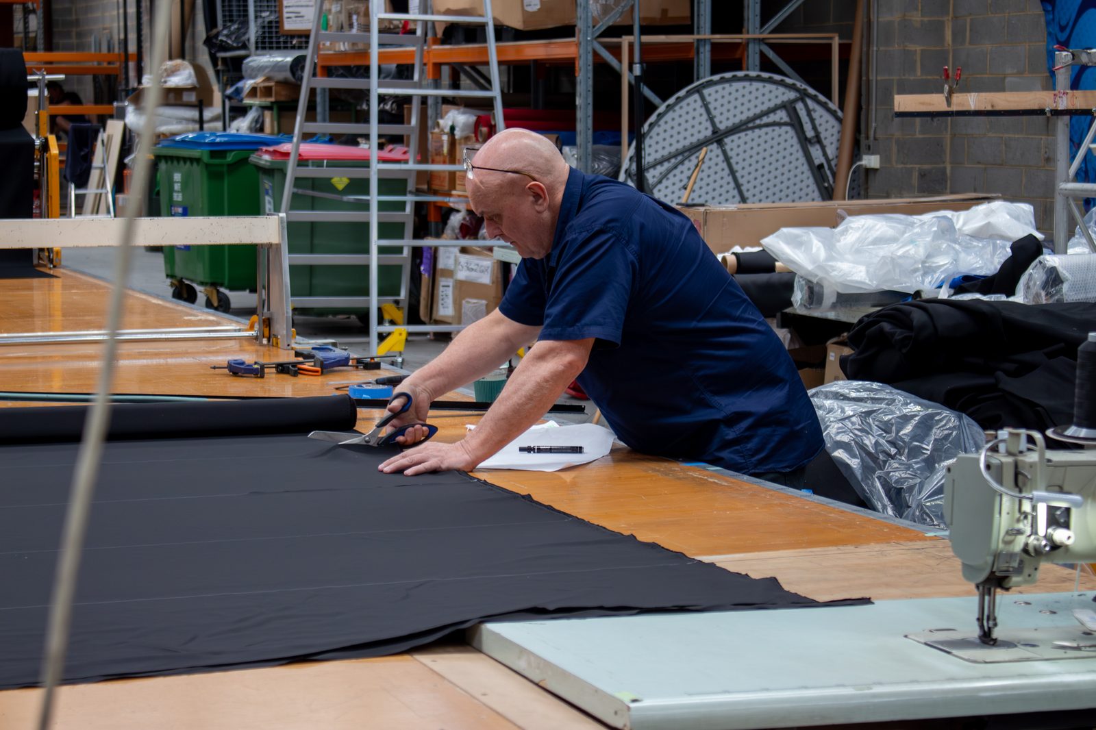 A machinist cutting black drape fabric with shears at the workshop table