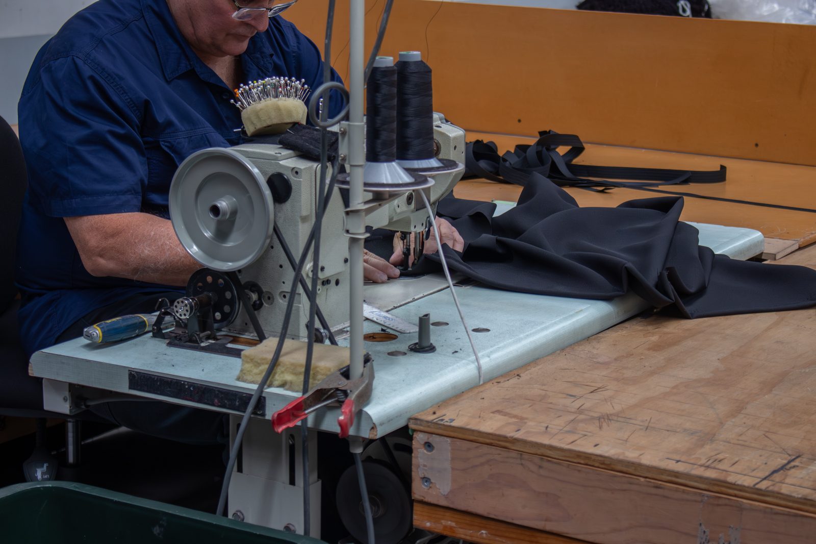 A machinist at an industrial sewing machine, feeding black drape fabric across the bench