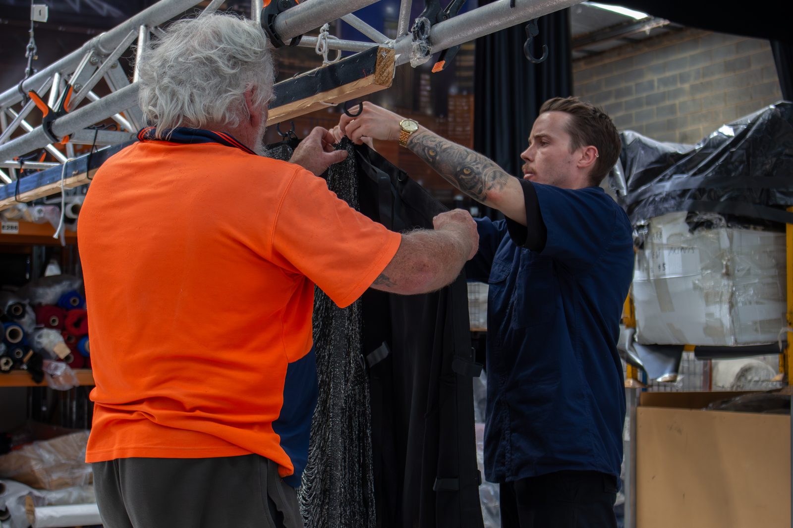 Two workshop staff hanging a black drape from a truss rig to check its drop