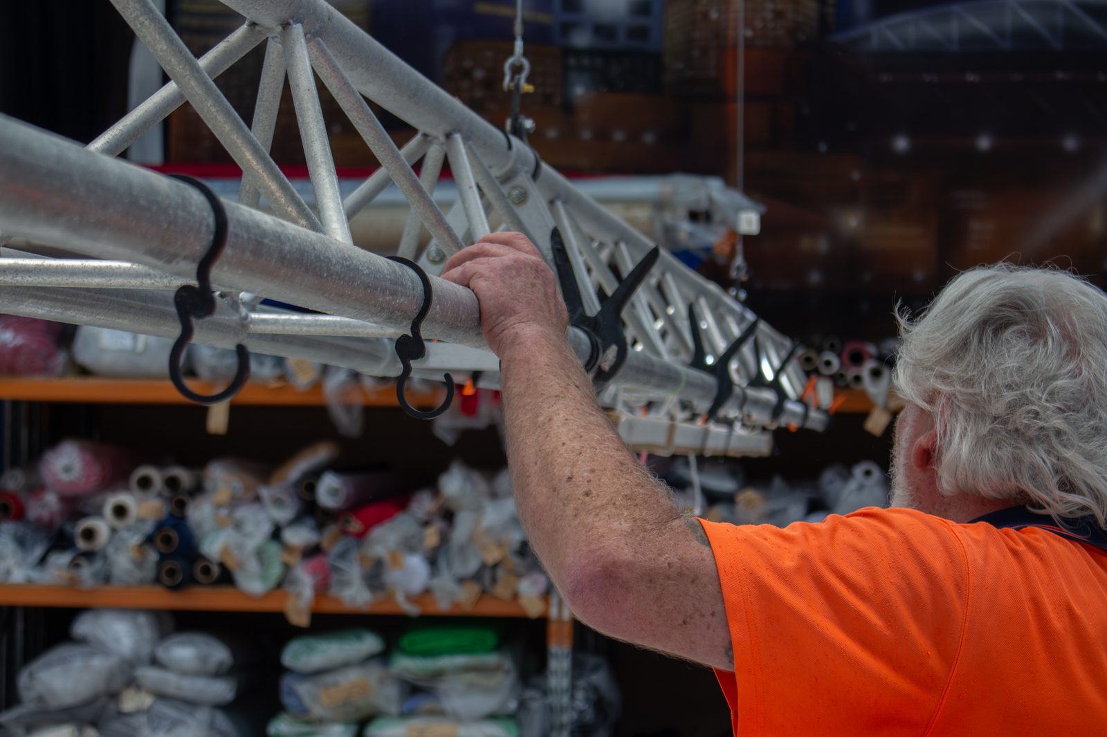 A technician clipping a drape's hooks onto a bar under the workshop truss