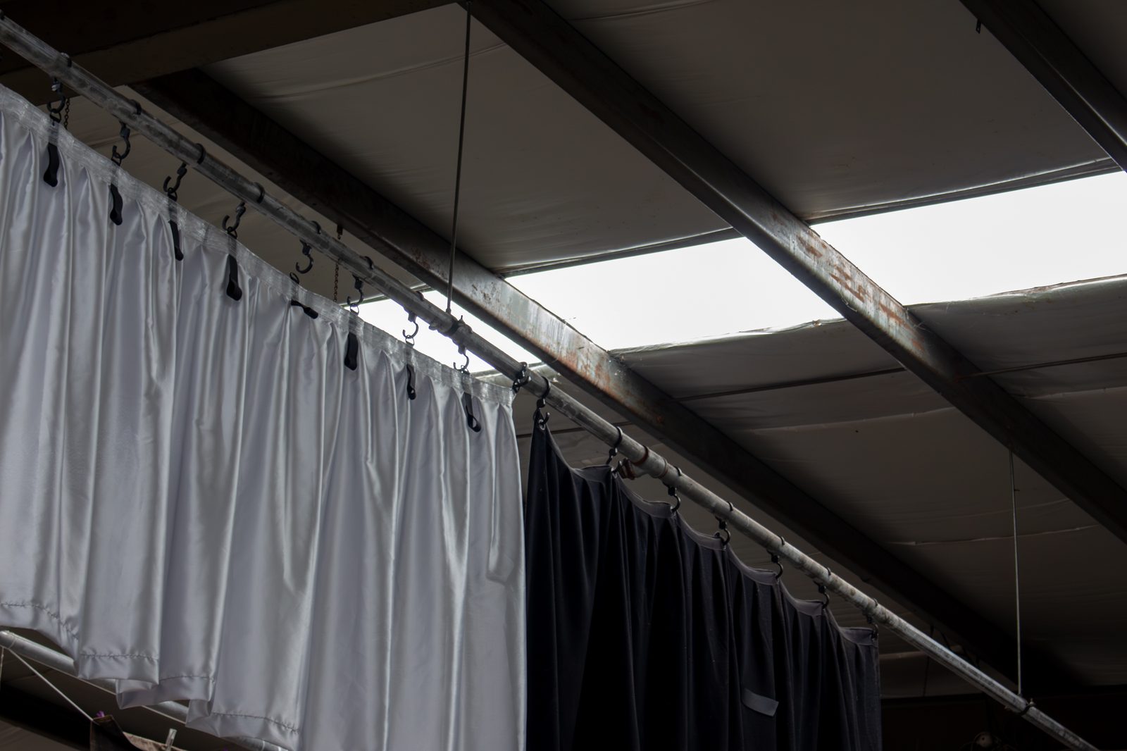 White and black drapes hanging from a pipe under the workshop skylights