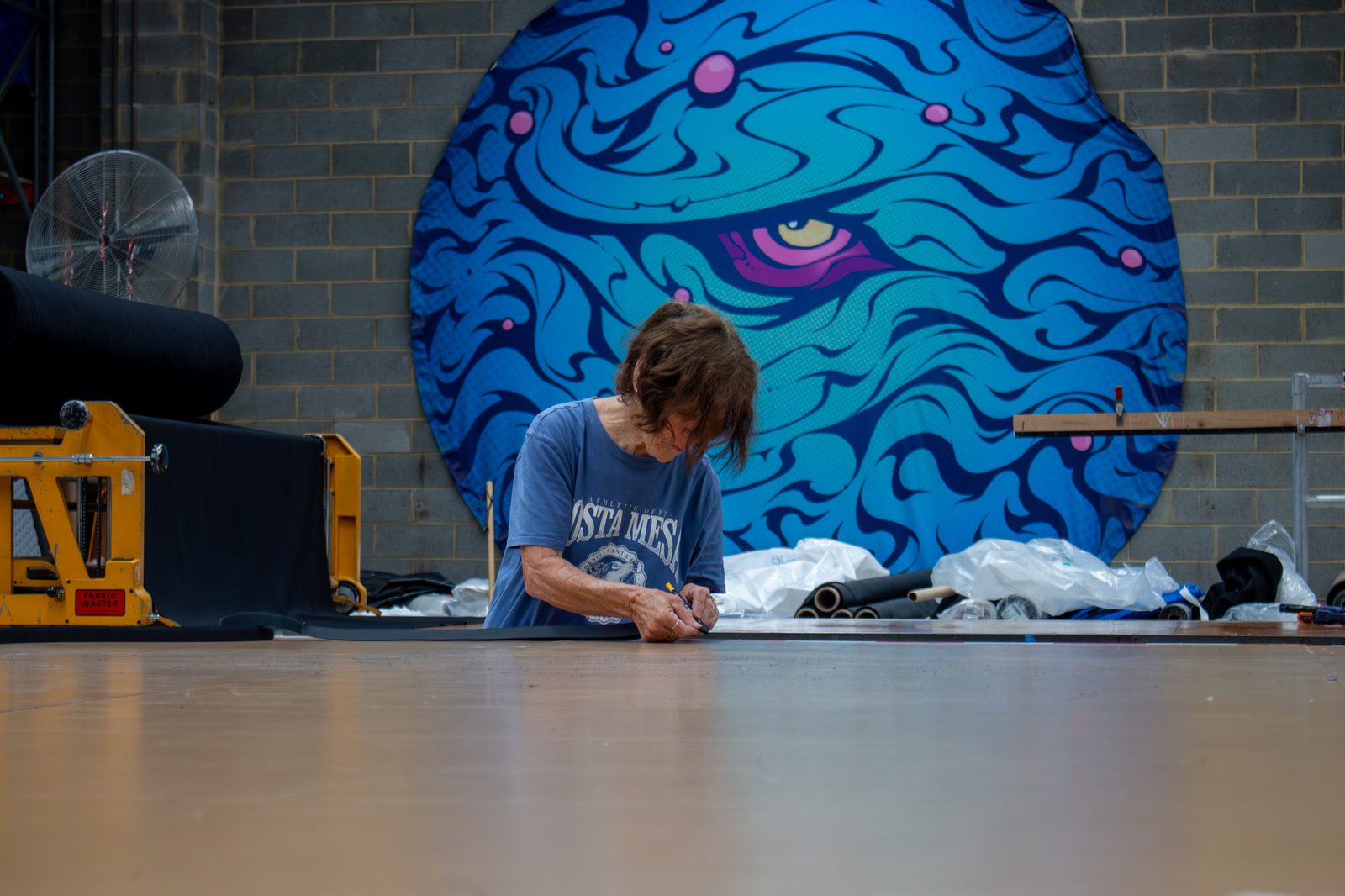 A machinist marking a hem on fabric laid across the workshop floor