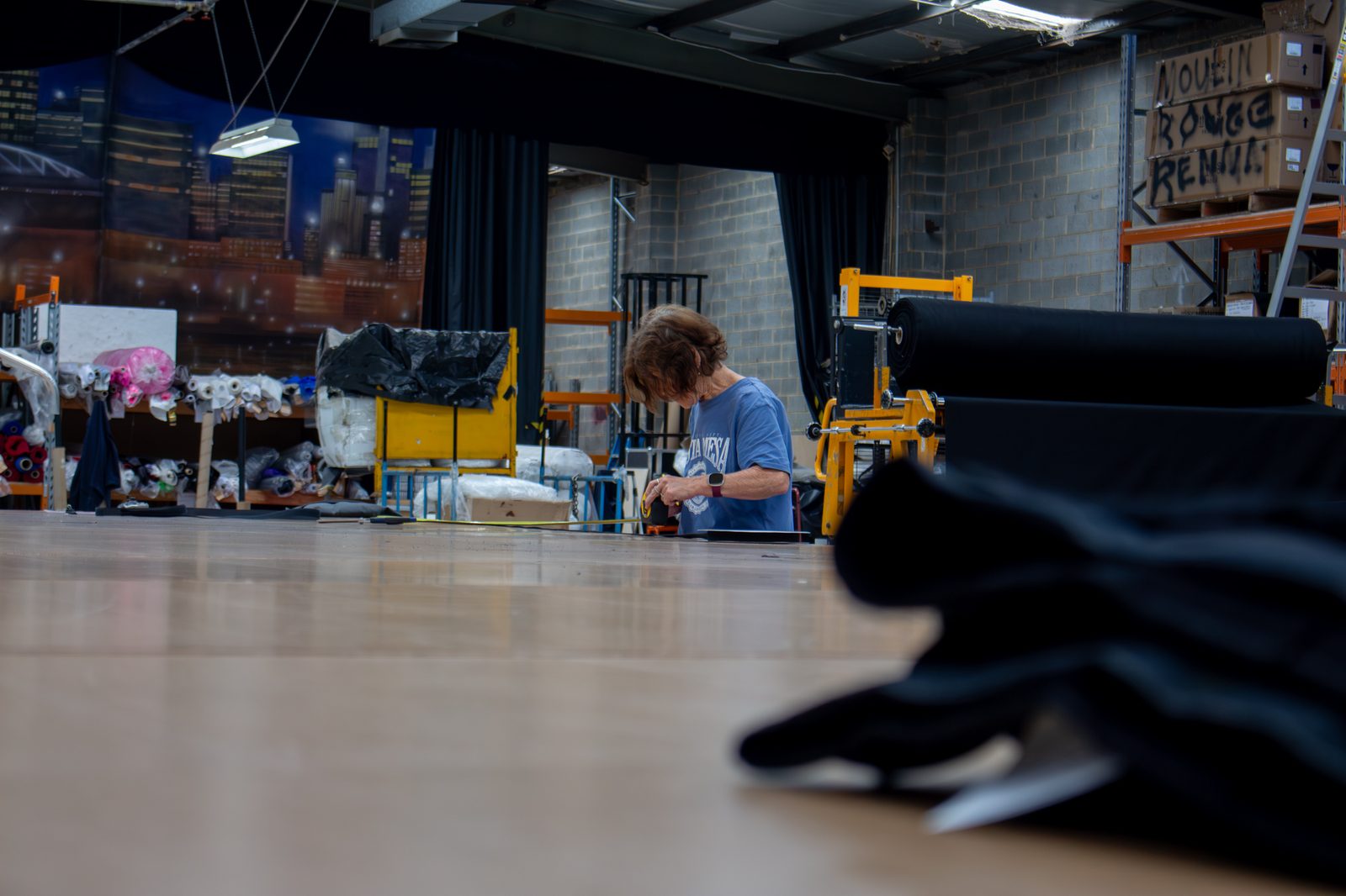 A maker at a long cutting table in the workshop, a roll of black drape in the foreground