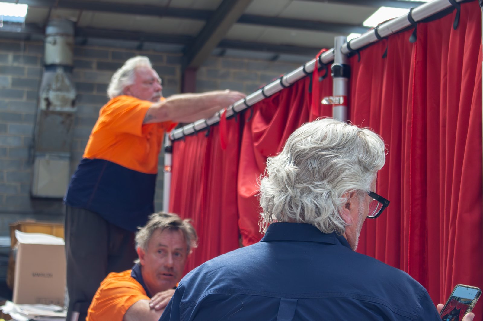 Red velvet drapes hung on a track in the workshop while three staff check the hang
