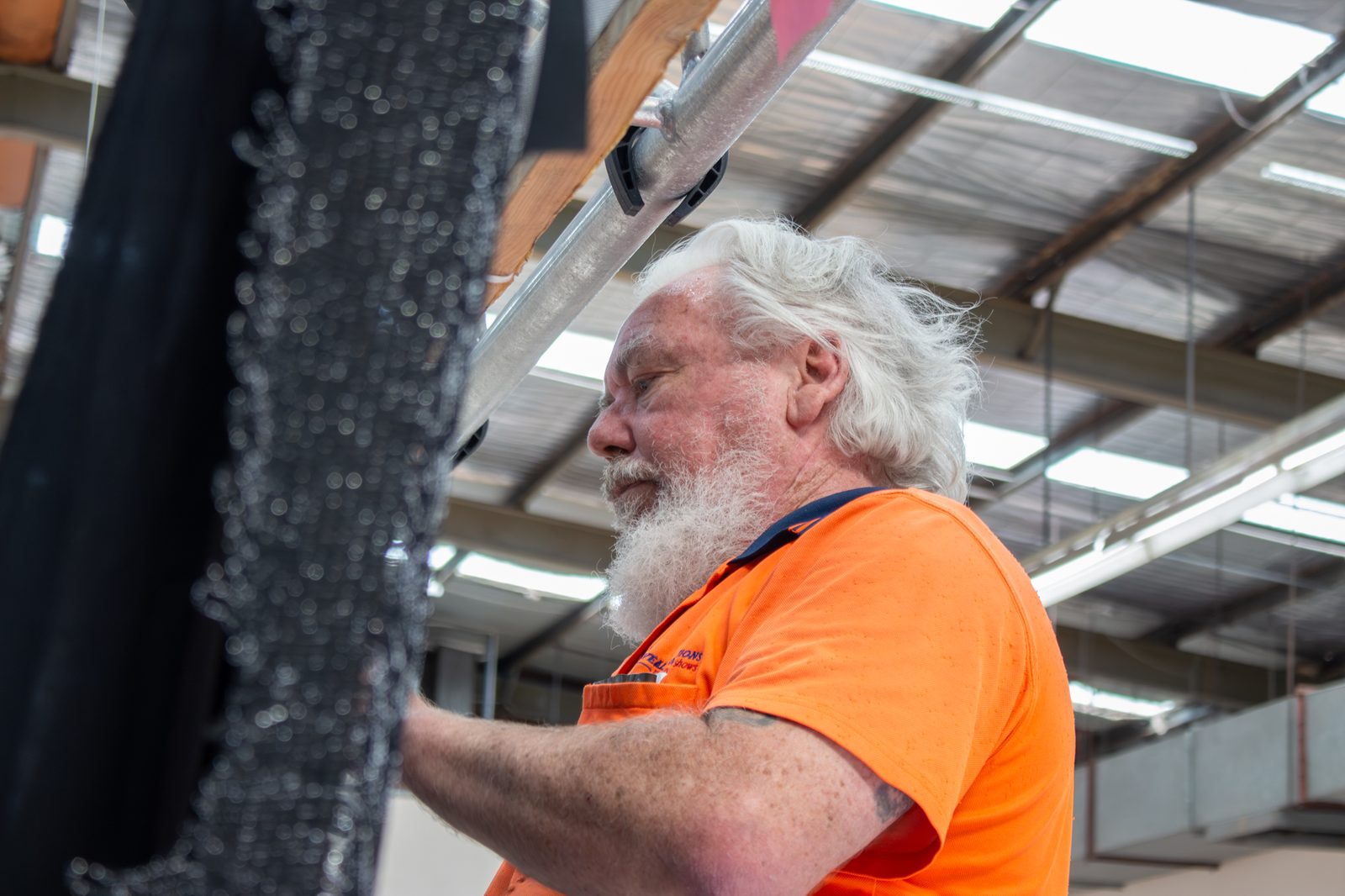A technician looking closely at a beaded black drape held up in the workshop
