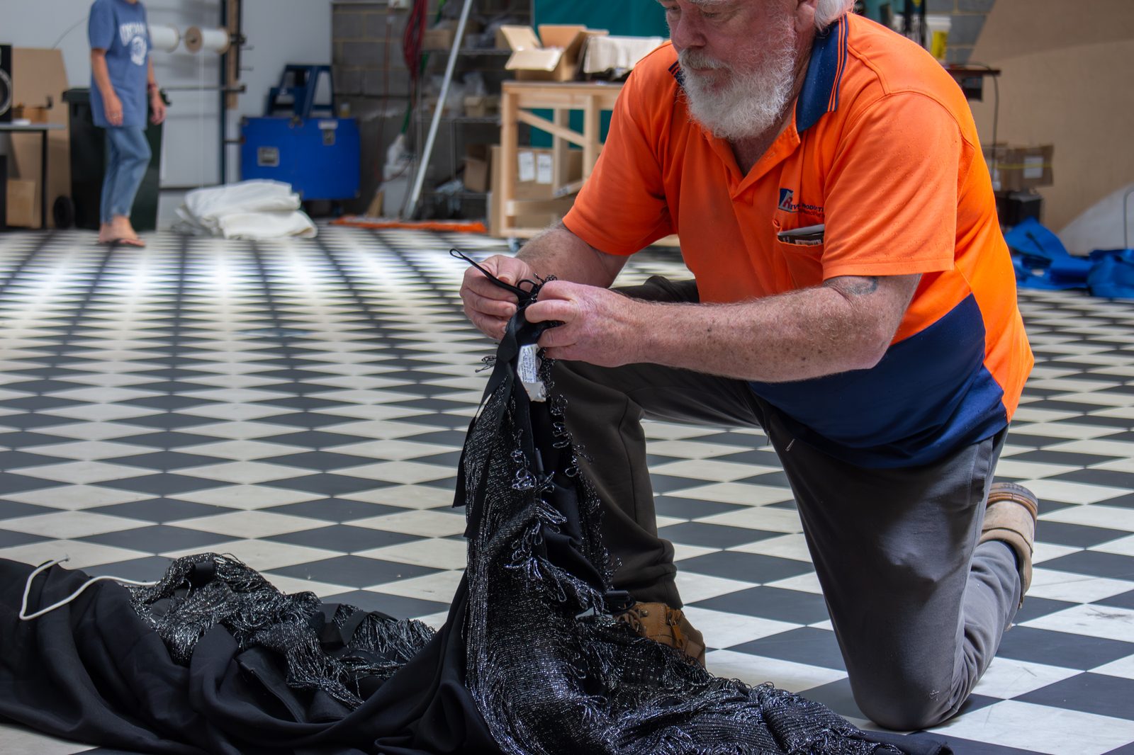A staff member kneeling on the chequered workshop floor, checking the heading and ties of a black drape