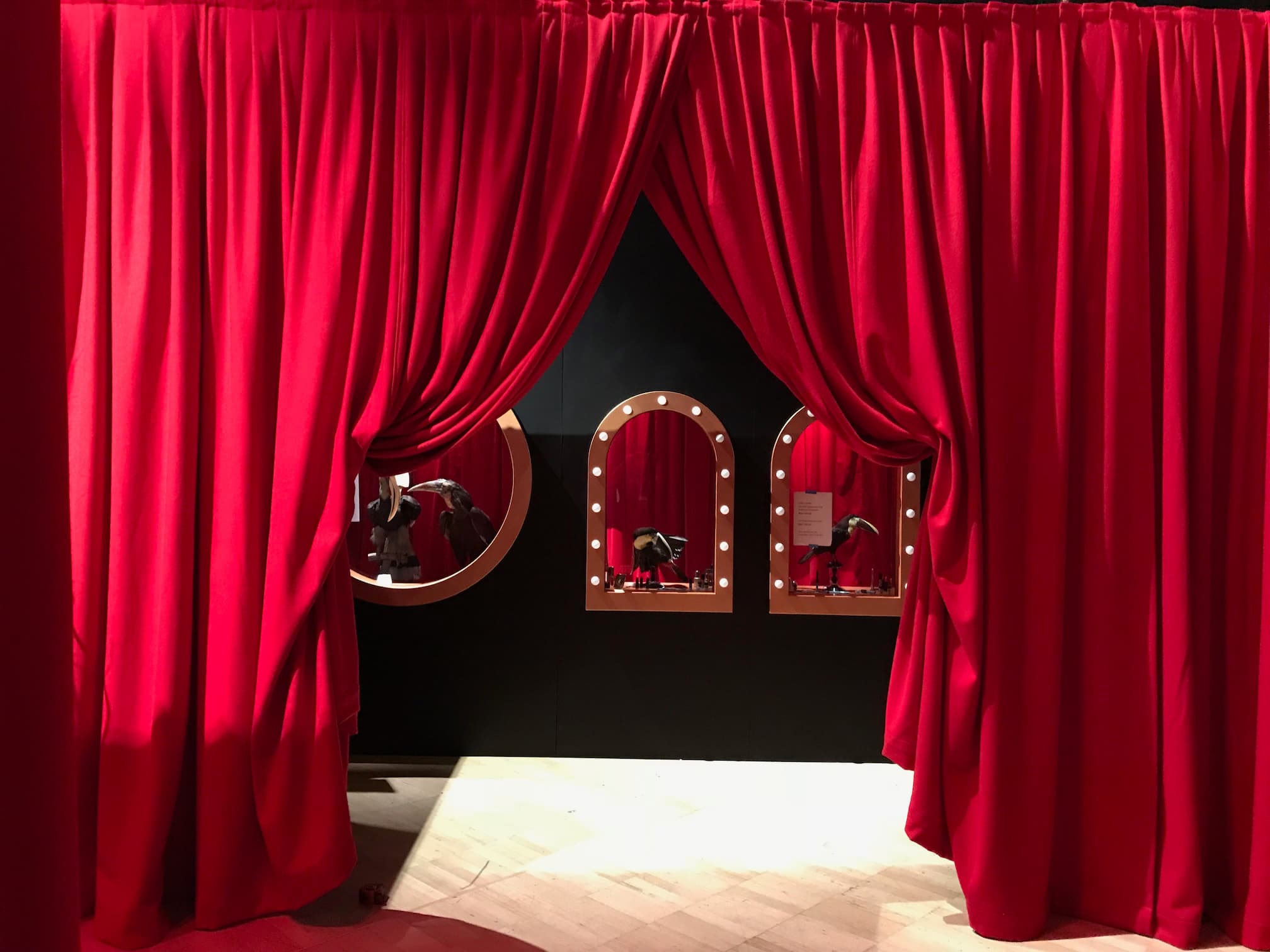 Red stage curtains drawn open at centre stage, revealing a black set wall with lamp-lit arched mirrors