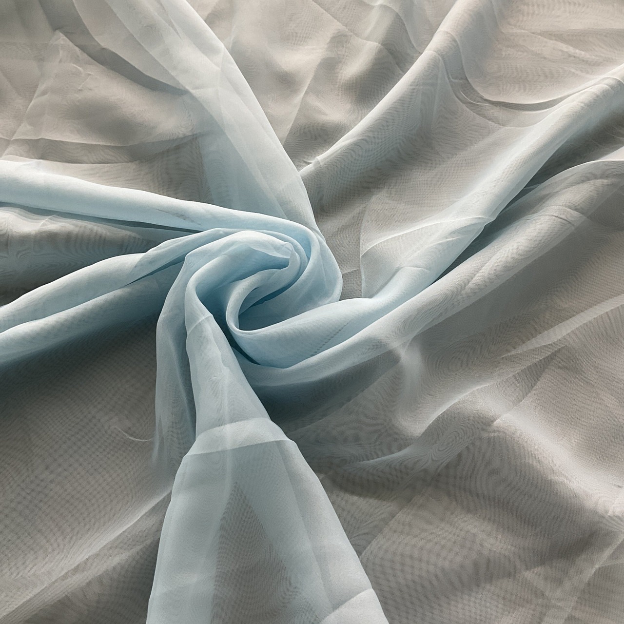 Pale blue sheer voile fabric gathered in soft folds, photographed in true colour