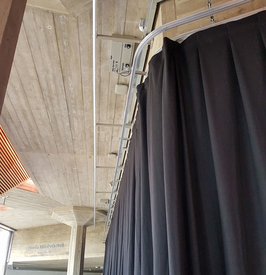 Aluminium walkalong track curving across a timber soffit, carrying a pleated black drape