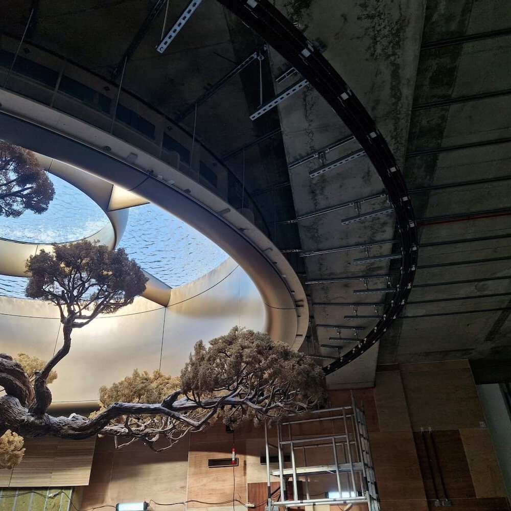 Heavy curved black track following an oval ceiling opening above a sculptural tree on a venue fit-out