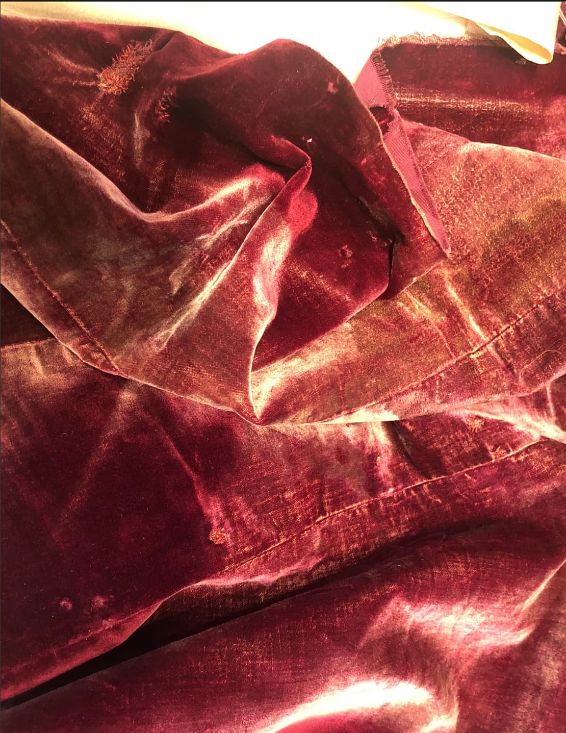Worn burgundy velvet drape with faded pile and visible wear at the seams