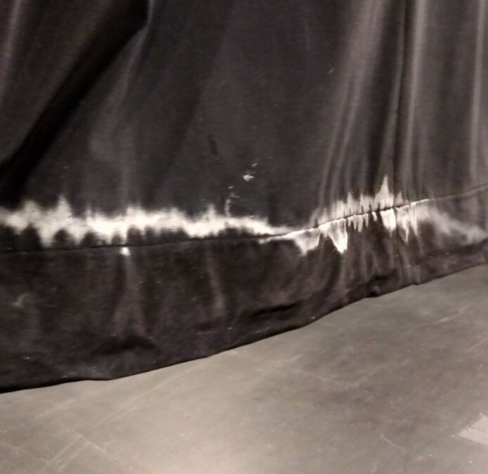 White tide marks along the hem of a black stage drape after water