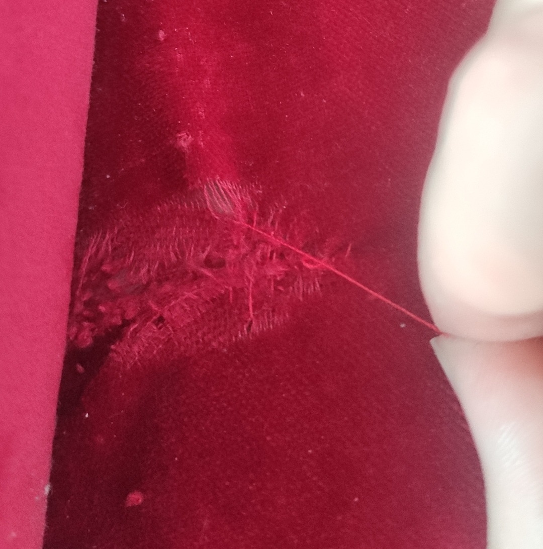 A pulled thread running out of damaged red velvet pile near a seam