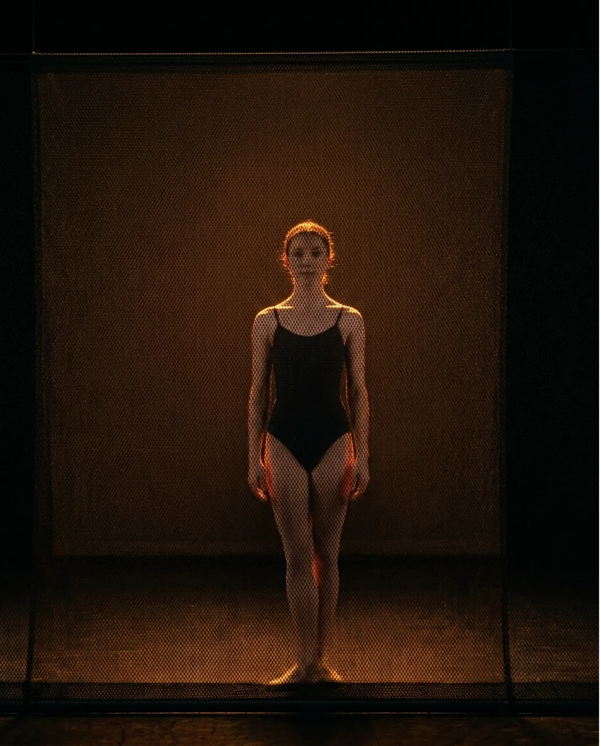 The same black sharkstooth scrim with the light behind it, now transparent, revealing the dancer standing upstage